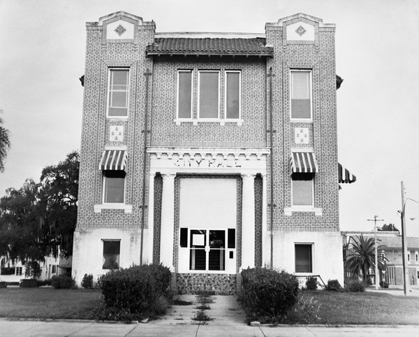 Black and white historical photo of an old two story brick city hall building with arched windows